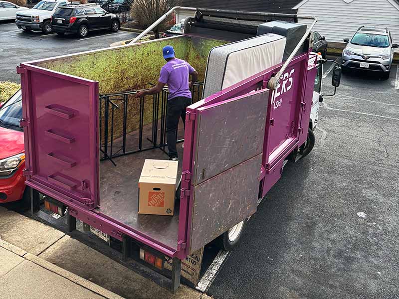 Junk Runners worker loading furniture into the back of a company truck for disposal.